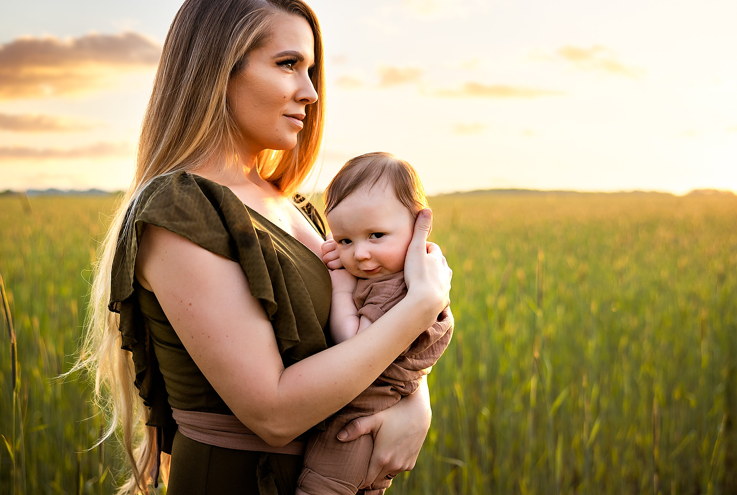 A mother holding her baby in a tall grass field at sunset