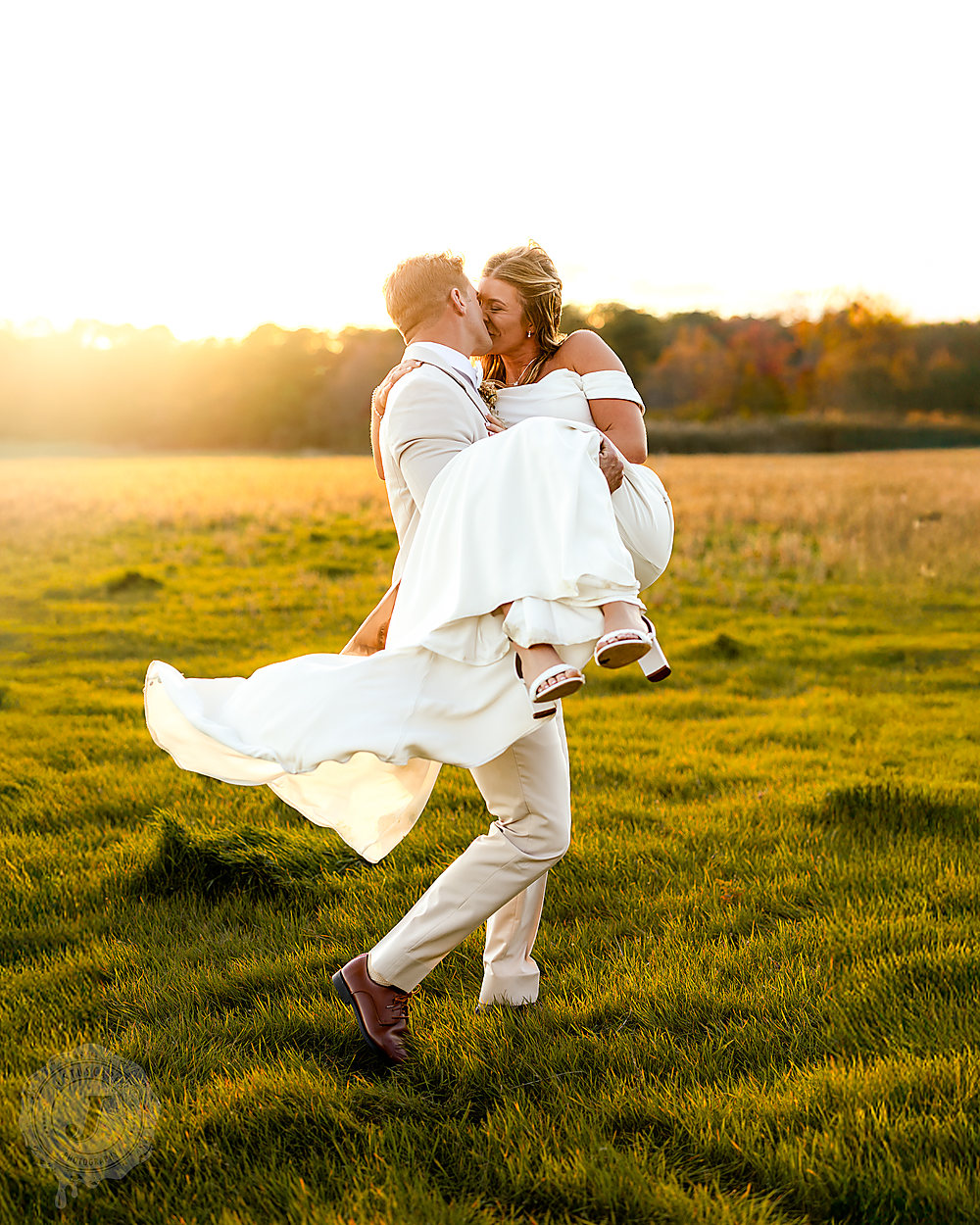 A groom carrying his bride across a field at golden hour