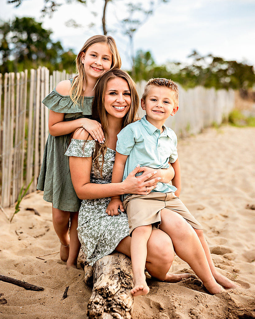A mom with her two kids on the sand by a beach fence