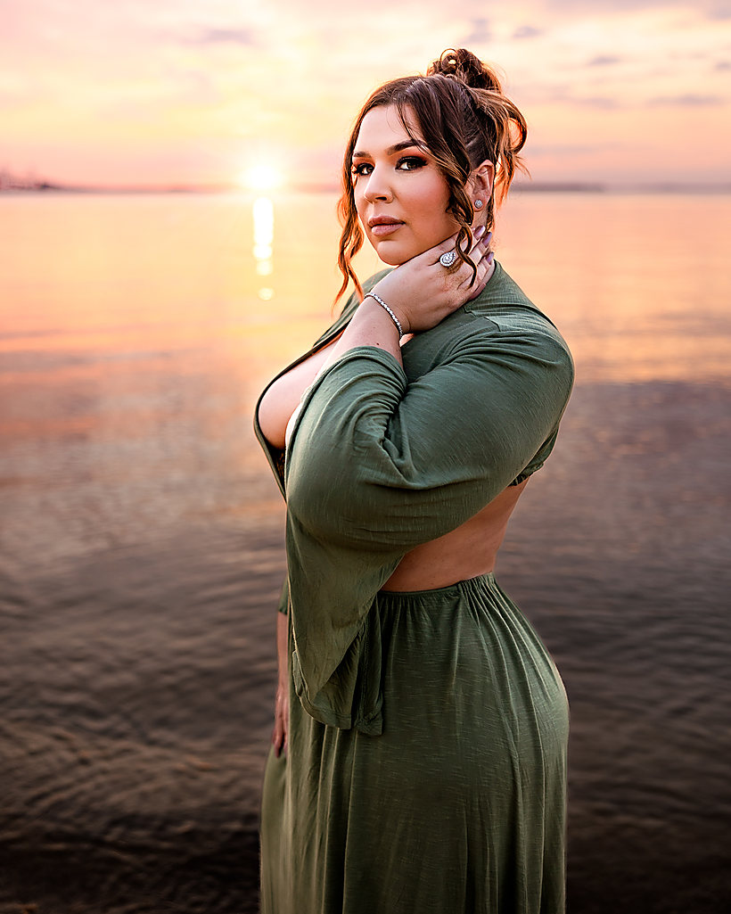 A woman in a green dress at the water at sunset