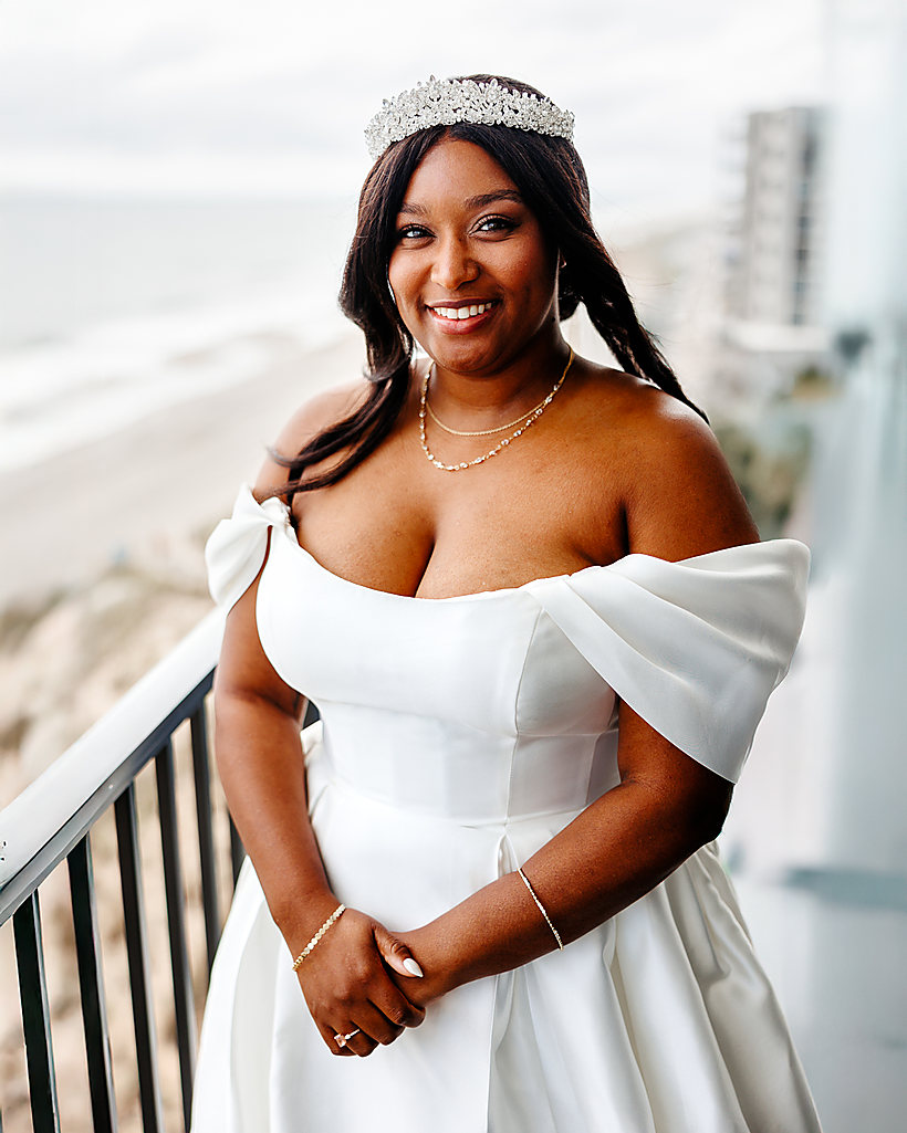 A smiling bride in a tiara on a balcony above the beach